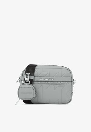 Pilka per petį nešama kuprinė, pagaminta iš tekstūrinės odos, turi užtrauktuką, logotipo akcentą ir reguliuojamą diržą su metalinėmis detalėmis.