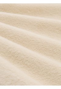 Tissu beige doux avec une texture duveteuse montré en gros plan, soulignant la chaleur et la surface moelleuse du matériau.