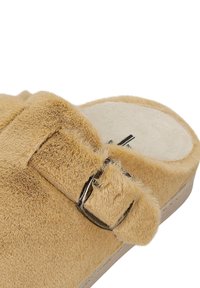 Tan, fuzzy instapsandaal met een ronde neus en verstelbare gesp, voorzien van een textuur bovenkant en een gladde, lichtgekleurde binnenzool.