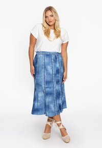 Jupe en denim de différentes nuances de bleu avec une silhouette évasée, des coutures verticales et une taille. Associée à un haut blanc à manches courtes.