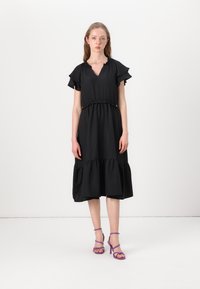 Black dress with short, ruffled sleeves, a V-neckline, elasticized waist, and tiered skirt. Worn with purple strappy heels.