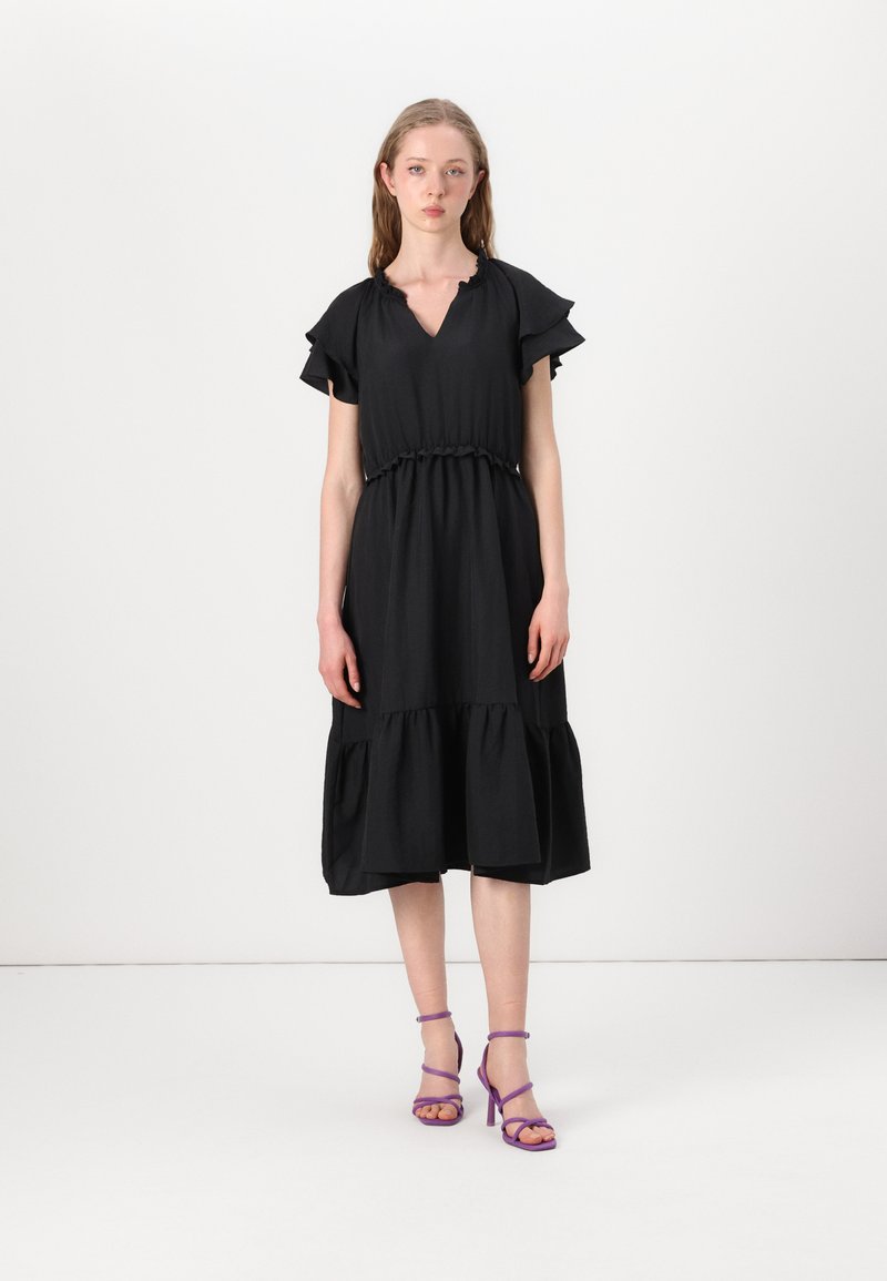 Black dress with short, ruffled sleeves, a V-neckline, elasticized waist, and tiered skirt. Worn with purple strappy heels.
