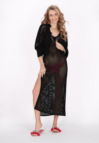 Czarna, otwarta sukienka zakrywająca z głębokim dekoltem w kształcie litery V i bocznym rozcięciem. Połączona z różowymi i czerwonymi: dekoracyjnymi klapkami z falbaniastymi akcentami.