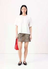 Hvit oversized t-skjorte med en teksturert lomme, kombinert med et geopardprint mini-skjørt, rød veske og svarte naglede flate sko.