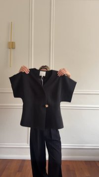 Black short-sleeve top made of a soft, textured fabric, featuring a loose fit, V-neck, and a single decorative button at the waist.