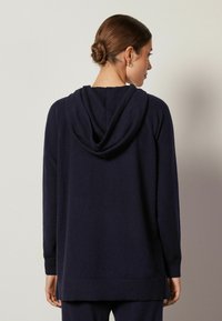 Marineblaues Kapuzensweatshirt aus weichem Material, mit einem lässigen Schnitt, gerippten Bündchen und einem längeren hinteren Saum. Glatte Textur.