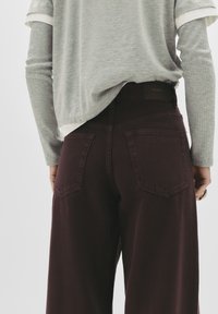 Bledi sivi dolgih rokavov nadvlečen na kratke rokave bele majice; visoko pasne temno burgundske široke hlače z dvema zadnjima žepoma.