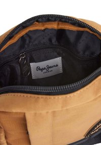Rudas audinys maišo vidus su juodu pamušalu, užtrauktukų uždarymas ir etikete, kurioje parašyta "Pepe Jeans London." Ypatybė - lygus paviršius.