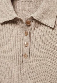 Polo shirt beige a coste con colletto e cinque bottoni rotondi color marrone chiaro. La texture appare morbida e lavorata a maglia.
