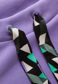 Tessuto viola con finitura testurizzata che presenta due cordini; uno di essi ha un motivo geometrico in bianco, nero e verde, aggiungendo un tocco di stile.