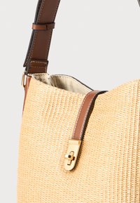 Gewebte Strohtasche mit beiger Textur, braunen Lederelementen und einem goldfarbenen Verschluss. Verfügt über eine breite Öffnung.