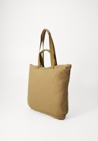 Brun kanvas tote bag med doble håndtak, rektangulær form, glidelås-lukking og minimal søm. Glatt tekstur og solid design.