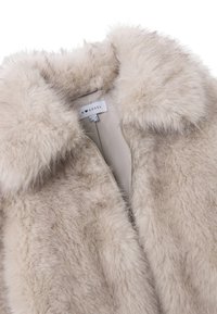 Nepbontvest in beige, met een zachte textuur, hoge kraag en ritssluiting. De binnenvoering is glad en toont het merklabel.