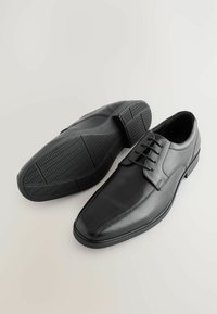 Zwarte leren dresschoenen met een puntige neus, vetersluiting en een rubberen zool met een gegroefd zigzagpatroon voor grip.