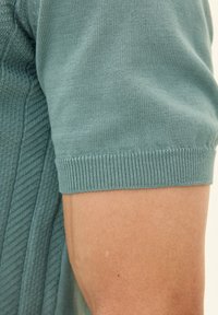 Lichtgroene gebreide shirt met korte mouwen, voorzien van geribbelde manchetten en gestructureerde zijpanelen met een gladde afwerking.