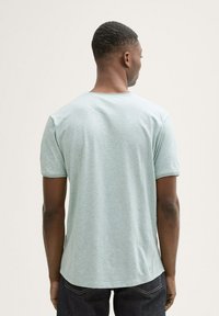 Camiseta de manga corta en verde agua con un cuello redondo, hecha de una tela suave y texturizada. El dobladillo tiene una forma ligeramente curva y cae a la altura de la cadera.