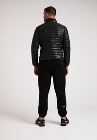 Giacca a vento nera con un design trapuntato, abbinata a pantaloni jogger neri. Presenta un colletto alto e polsini elastici. Scarpe sportive completano il look.