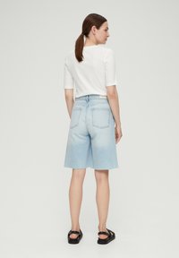 Lichtblauwe denim shorts met een relaxte pasvorm, ruwe zoom en twee achterzakken. Gecombineerd met een wit, aansluitend, kort mouwtopje en zwarte sandalen.