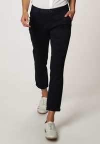 Chinos w kolorze granatowym o dopasowanym kroju, z bocznymi kieszeniami i podwiniętymi mankietami, w zestawieniu z białymi butami casualowymi o fakturowanym wykończeniu i przeszyciach.