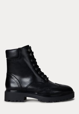 Black leather ankle boot with a round toe, brogue detailing, flat lace-up design, and a chunky rubber sole. Features a padded collar.