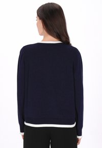 Laivastonsininen neulepaita, jossa on valkoinen ribbineuloskaulus ja helma, pitkät hihat ja rento istuvuus. Pehmeä pinta ja minimalistinen muotoilu.