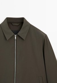 Mørkeolivengrøn zip-up jakke med spids krave og synlig metallynlås på en ensfarvet hvid baggrund.