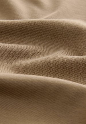 Beige stof med en glat tekstur, der viser et subtilt ribbet mønster. Materialet ser blødt ud og falder i bløde folder.