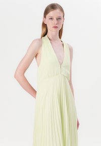 Abito senza maniche con scollatura a V profonda in verde lime chiaro, caratterizzato da pieghe verticali e un design fluido, realizzato in tessuto leggero.