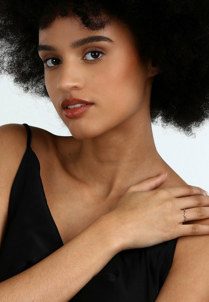 Schwarzes Satin-Kleid mit dünnen Trägern, Model mit lockigem schwarzen Haar, trägt einen silbernen Ring an der rechten Hand, helle Hautfarbe und neutrales Make-up.
