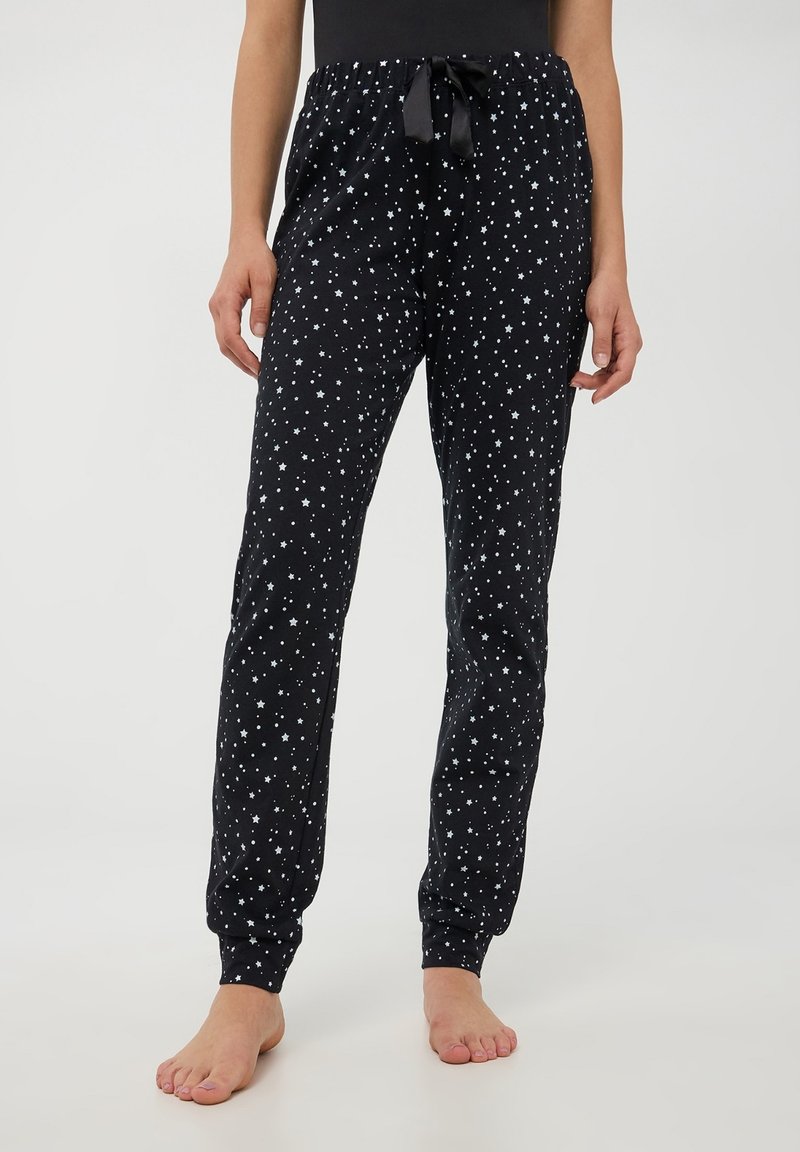 Pantaloni da pigiama neri con stampa di stelle bianche, vita con cordino, polsini elastici e una texture morbida. Presentano una vestibilità rilassata per il massimo comfort.