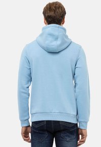 Hellblaues Hoodie aus weichem Material. Verfügt über eine Kapuze mit Zugband und gerippte Bündchen, kombiniert mit dunkelblauen Jeans. Rückansicht.