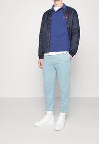 Marinblå kviltad bomberjacka, blå polo-tröja, ljusblå sweatpants och vita sneakers med texturerad yta och ribbade mudd.