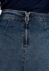 Jeansrock mit hohem Bund, ausgestattet mit einem Reißverschluss vorne, in dunkler blauer Waschung und kontrastierendem orangenem Stich entlang der Nähte.