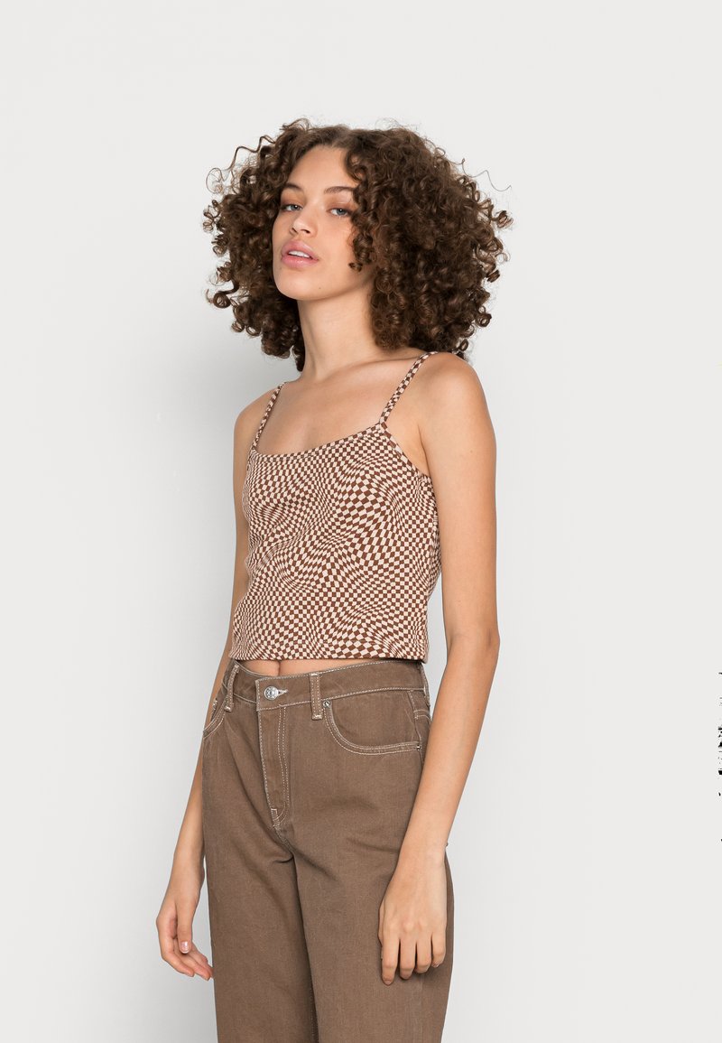 Top cropped em padrão xadrez castanho e branco, com alças finas e detalhes franzidos, combinado com calças castanhas de cintura alta. Textura de tecido suave.