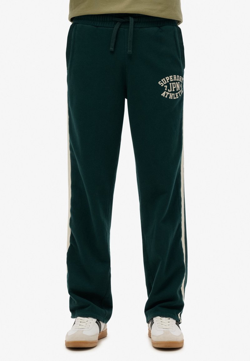 Donkergroene sweatpants met een trekkoord in de taille, zijstrepen in crème en de opdruk "Superdry JPN Athletic" aan de voorkant. Zacht, comfortabel materiaal.