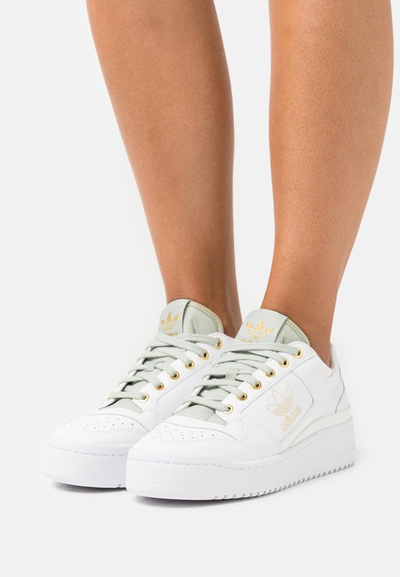 Sneakers bianchi in pelle con una finitura testurizzata, accenti verde chiaro, occhielli dorati e suola piatta bianca. Logo sul lato e sulla linguetta.