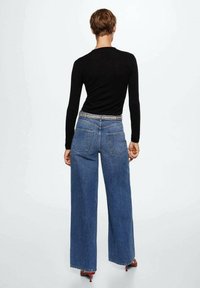 Un haut noir à manches longues et un jean bleu taille haute à jambes larges avec un lavage léger, comportant des poches arrière et une coupe droite.