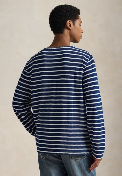 Μακρυμάνικη ριγέ μπλούζα σε ναυτικό μπλε και λευκό. Βαμβακερό ύφασμα, άνετη εφαρμογή, στρογγυλή λαιμόκοψη, με οριζόντιες ρίγες και ανοίγματα στα πλάγια στο τελείωμα.