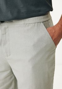 Pantalones de lino gris claro con cinturilla elástica, bolsillos laterales y una textura suave. Presenta líneas limpias y un ajuste casual.