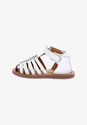 Sandalia de piel blanca con diseño de punta abierta, múltiples correas y cierre de Velcro ajustable. Suela marrón con acabado texturizado.