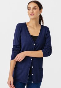 Cardigan blu navy realizzato in tessuto morbido con scollatura a V, chiusura con bottoni e due tasche frontali. Presenta maniche lunghe e bordo a coste.