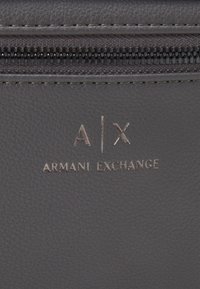 Szara skórzana tkanina o teksturowanej powierzchni. Zawiera srebrne wytłoczone logo „A|X ARMANI EXCHANGE” oraz zamek błyskawiczny na górze.