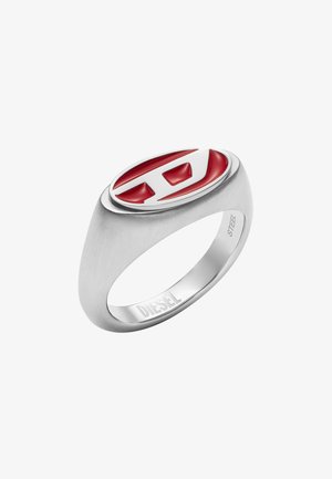 Silverfärgad ring av rostfritt stål med en slät matt finish. Har en oval röd emaljinläggning och ett utskuret logotyp i vitt. Varumärket graverat på insidan.