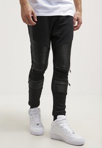 Svarta joggerbyxor med strukturerade svarta paneler, med blixtlås och ribbade detaljer. Matchas med vita högre sneakers.