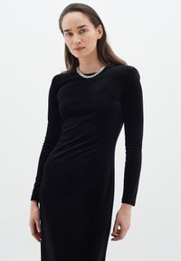 Long-sleeved black velvet dress featuring a fitted silhouette, round neckline adorned with metallic accents, and smooth, soft texture.