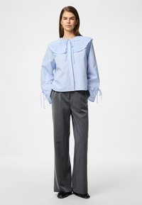 Ανοιχτό μπλε ριγέ μπλούζα με μεγάλη, φουσκωτή κολάρο και λεπτομέρειες από κορδόνι, συνδυασμένη με γκρίζες παντελόνες σε φαρδιά γραμμή. Λείο υλικό.