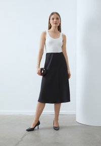 Ærmeløs hvid top med en sort midi-nederdel. Glat stof med en afslappet silhuet. Sorte spidse hæle og en clutch i skildpaddemønstret.