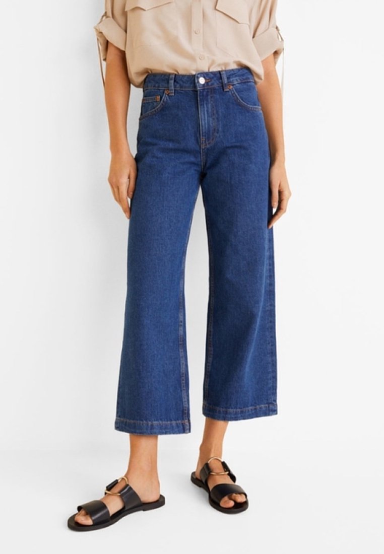 Pantalones de denim de pierna ancha en azul oscuro, de cintura alta, con un diseño clásico de cinco bolsillos y costuras en contraste, combinados con sandalias negras.