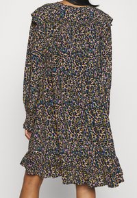 Femme portant une robe à manches longues, jusqu'aux genoux, avec un motif floral abstrait multicolore et un ourlet volanté, vue de dos.