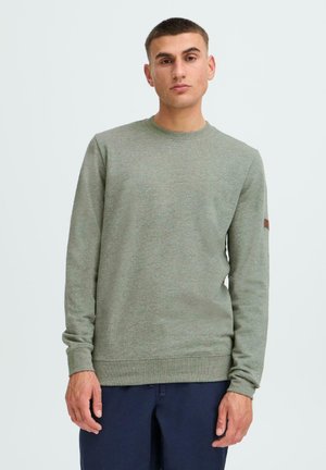 Green crew-neck sweatshirt made of textured fabric, featuring long sleeves and a brown brand accent on the left shoulder.